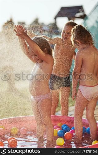 Little cute adorable kids enjoying a cool water sprayed by their father during hot summer day in backyard. Candid people, real moments, authentic situations