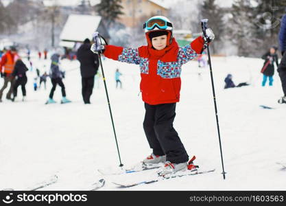 Little cute boy with skis and a ski outfit. Little skier in the ski resort. Winter holidays. Skiing