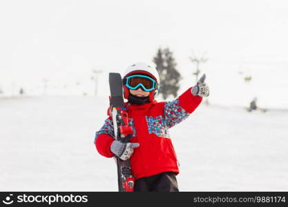 Little cute boy with skis and a ski outfit. Little skier in the ski resort. Winter holidays. Skiing