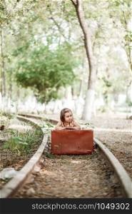 little cute Caucasian girl in vintage clothes with vintage suitcase on abandoned railway