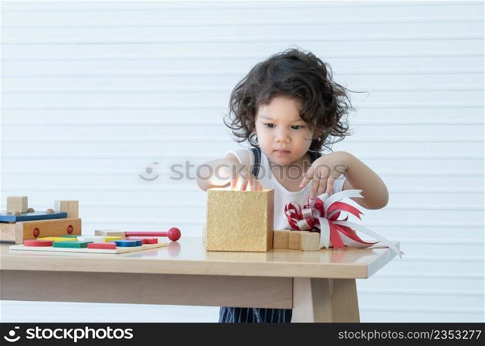 Little cute Caucasian kid girl is having fun to open gold gift box in living room at home while playing toys. Adorable daughter received a surprise gift for her birthday.