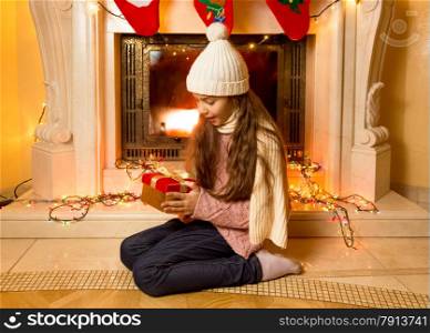 Little cute girl looking at Christmas gift at fireplace