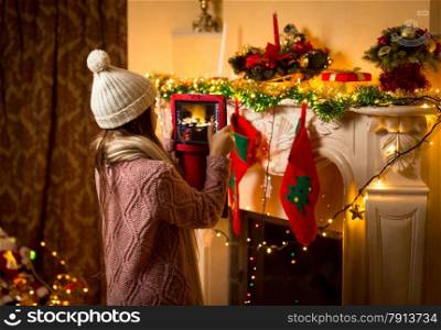Little cute girl making photo of decorated Christmas fireplace on digital tablet