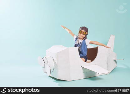 Little cute girl playing with a cardboard airplane. White retro style cardboard airplane on mint green background . Childhood dream imagination concept .