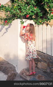 Little cute girl portrait outdoors in old greek village. Kid at street of typical greek traditional village with white walls and colorful doors on Mykonos Island, in Greece. Girl in white dresses having fun outdoors on Mykonos streets