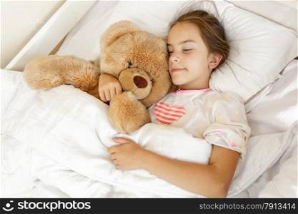 Little cute girl sleeping and hugging big teddy bear at bed