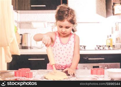 Little cute girl stretching the dough in the kitchen. Happy little chef