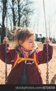 Little cute girl swinging in a park on sunny spring day. Child wearing red jacket