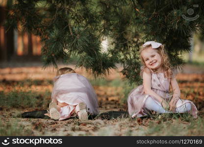 little cute girls have fun under the tree on a sunny spring day. children collect cones.. little cute girls have fun under the tree on a sunny spring day. children collect cones