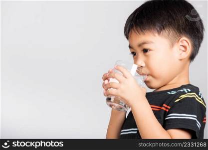 Little cute kid boy 5-6 years old smile drinking fresh water from glass in studio shot isolated on white background, Asian children preschool, Daily life health