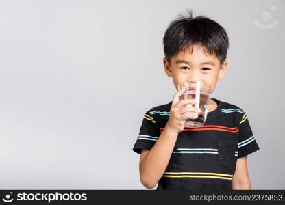 Little cute kid boy 5-6 years old smile drinking fresh water from glass in studio shot isolated on white background, Asian children preschool, Daily life health