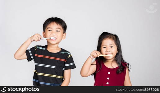 Little cute kid boy and girl 3-6 years old brushing teeth and smile in studio shot isolated on white background, happy Asian children holding toothbrush in mouth by himself, Dental hygiene healthy