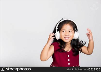 Little cute kid girl 3-4 years old listen music in wireless headphones in studio shot isolated on white background, happy Asian children smiling listening audio, entertainment lifestyle