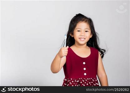 Little cute kid girl 3-4 years old show brush teeth and smile in studio shot isolated on white background, happy Asian children holding toothbrush in mouth by himself, Dental hygiene healthy concept