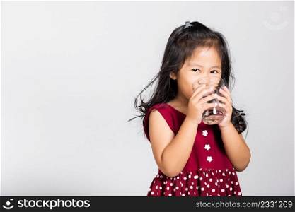 Little cute kid girl 3-4 years old smile drinking fresh water from glass in studio shot isolated on white background, Asian children preschool, Daily life health