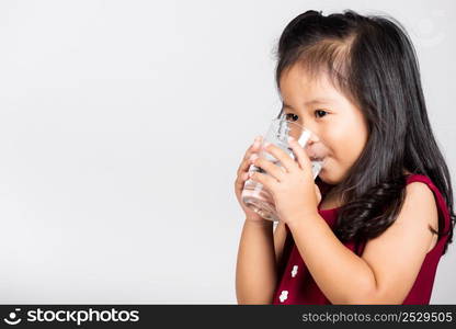 Little cute kid girl 3-4 years old smile drinking fresh water from glass in studio shot isolated on white background, Asian children preschool, Daily life health