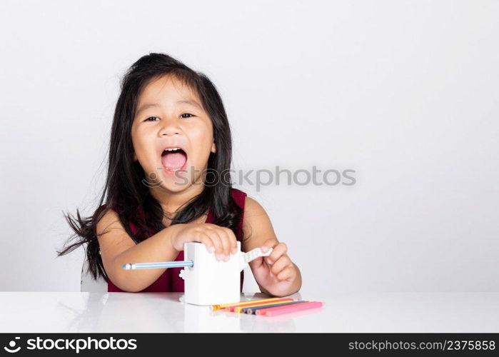 Little cute kid girl 3-4 years old smile using pencil sharpener while doing homework in studio shot isolated on white background, Asian children preschool sharpening color pencils, education concept