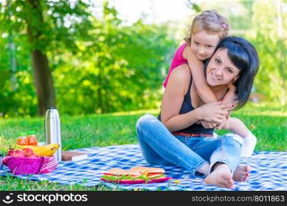 little daughter hugging her mother relaxing in the park
