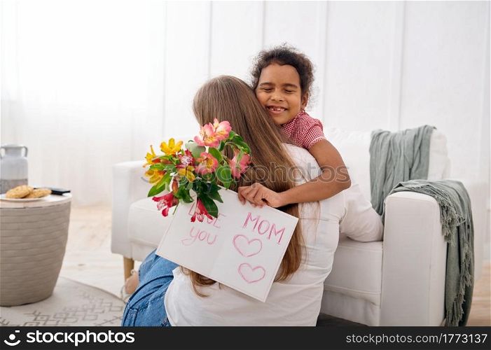 Little daughter wishes her beloved mother a happy birthday in living room.Mom and female child embracing, good relationship, parental care and love. Daughter wishes her beloved mother, happy birthday