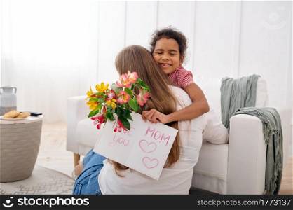 Little daughter wishes her beloved mother a happy birthday in living room.Mom and female child embracing, good relationship, parental care and love. Daughter wishes her beloved mother, happy birthday
