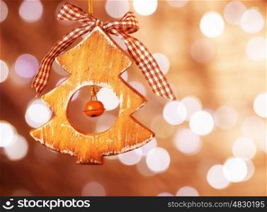 Little decorative wooden Christmas tree toy hanging on blurry shiny background, traditional Christmastime ornament
