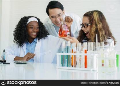 Little diversity African black and Caucasian children learning chemistry in school laboratory. Teacher man and clever girls doing a chemical science experiment in a laboratory on white background