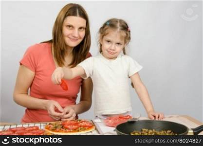 Little five-year girl helps mother spread on the pizza ingredients