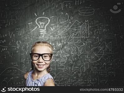 Little genius. Little cute girl of school age in glasses against blackboard