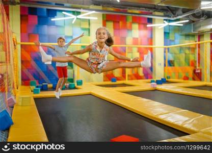Little girl and boy having fun on kids trampoline, playground in entertainment center. Play area for children indoors, playroom