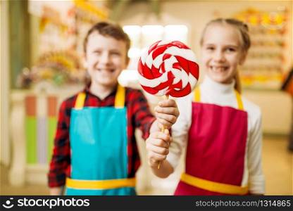 Little girl and boy holds in hands fresh lollipop. Children in workshop at pastry shop learn to make handmade caramel. Holiday fun in candy store