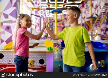 Little girl and boy play air hockey in entertainment center. Children having fun, kids sport competition on playground, happy childhood. Little girl and boy play air hockey on playground