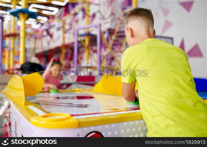 Little girl and boy play air hockey in entertainment center. Children having fun, sport competition on playground, happy childhood. Girl and boy play air hockey, entertainment center