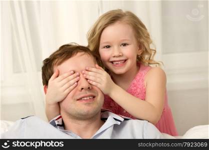 Little girl and father having fun together. She making a joke or playing hide-and-seek by closing his eyes