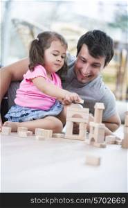 Little girl and father playing with wooden building blocks on floor