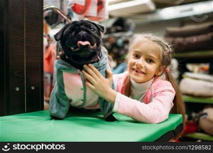 Little girl and funny puppy in clothes, pet shop. Kid and dogs in petshop, goods for domestic animals