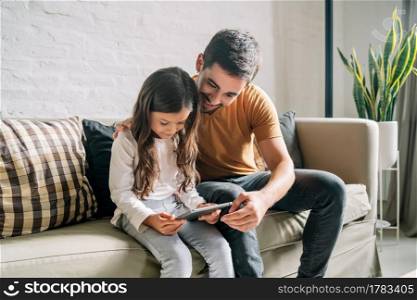 Little girl and her father having fun together while playing with a digital tablet at home. Monoparental family concept.