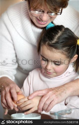 Little girl and her grandmother cracking an egg