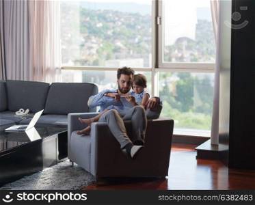 little girl and her handsome father using a digital tablet and smiling, sitting on couch at home