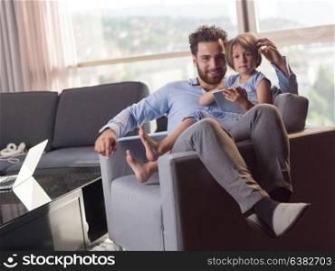 little girl and her handsome father using a digital tablet and smiling, sitting on couch at home