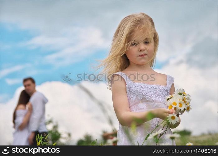 Little girl and his parents at blury background on camomile meadow at nature. Children pick flowers. Social and family problem.