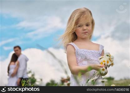 Little girl and his parents at blury background on camomile meadow at nature. Children pick flowers. Social and family problem.