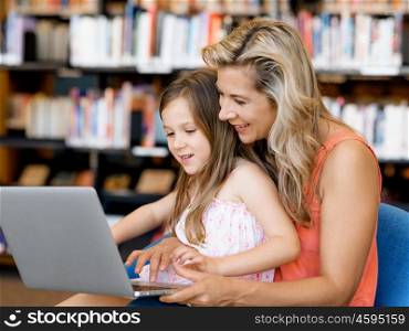 Little girl and mother with a laptop in library. Technology and fun in the library