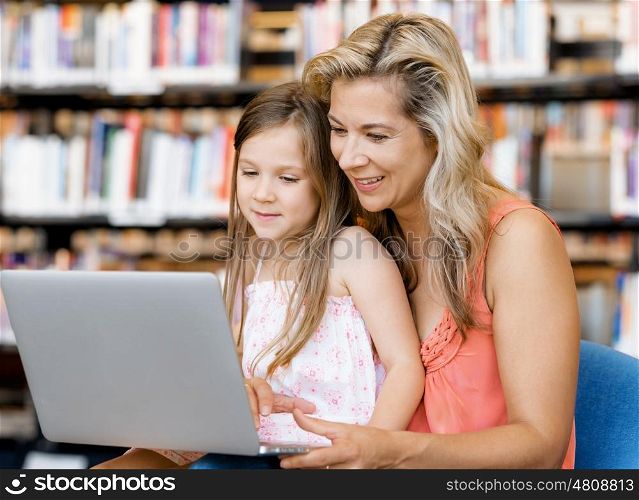 Little girl and mother with a laptop in library. Technology and fun in the library