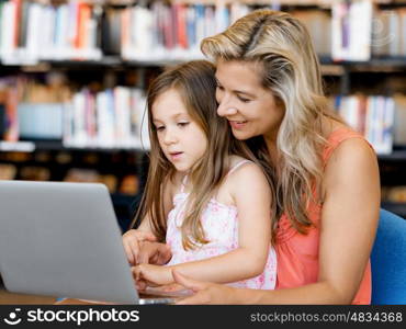 Little girl and mother with a laptop in library. Technology and fun in the library