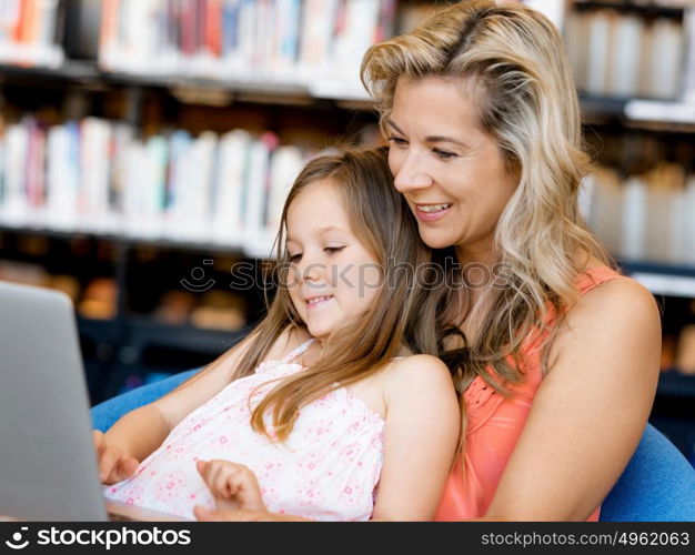 Little girl and mother with a laptop in library. Technology and fun in the library