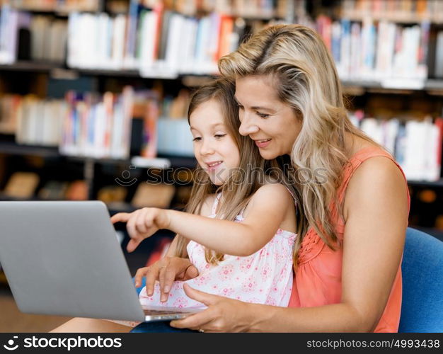 Little girl and mother with a laptop in library. Technology and fun in the library