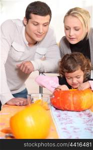 Little girl and parents carving pumpkin for Halloween