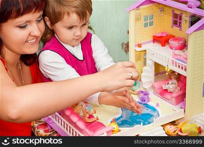 Little Girl and woman washes a doll in pool of toy house