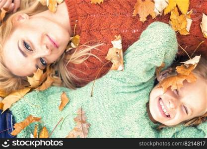 Little girl and young caucasian mom lying down directly above looking at camera on autumn leaves. Girl and mom lying on autumn leaves
