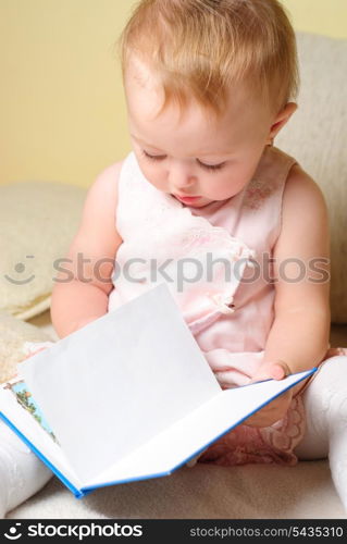 Little girl are readign the book, sitting on the sofa